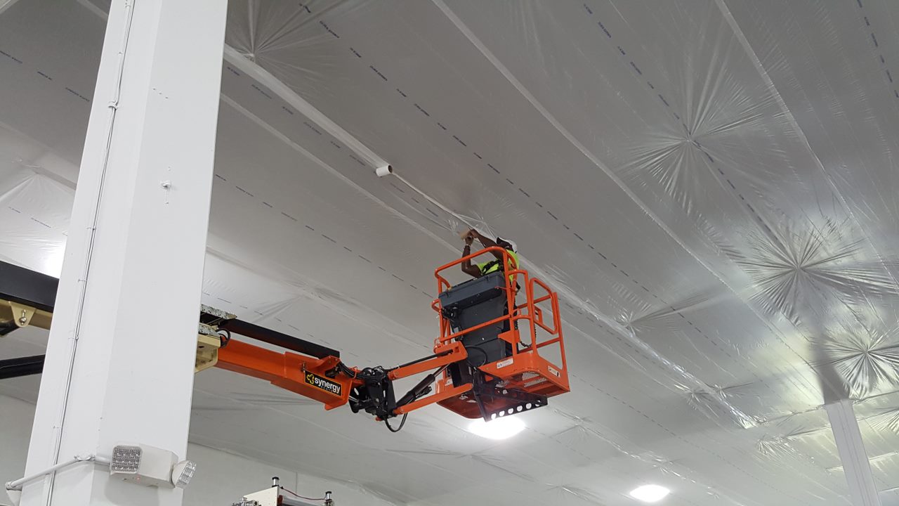 A man in an orange cherry-picker is working on the ceiling.